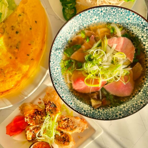 A vibrant Vietnamese meal with pho, banh xeo, and spring rolls on a white table.