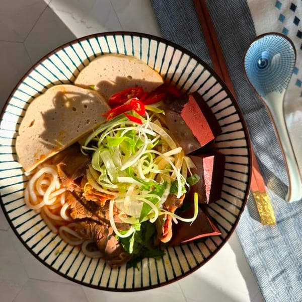 A bowl of Vietnamese Bun Bo Hue with noodles, sliced meat, red chilies, and greens.