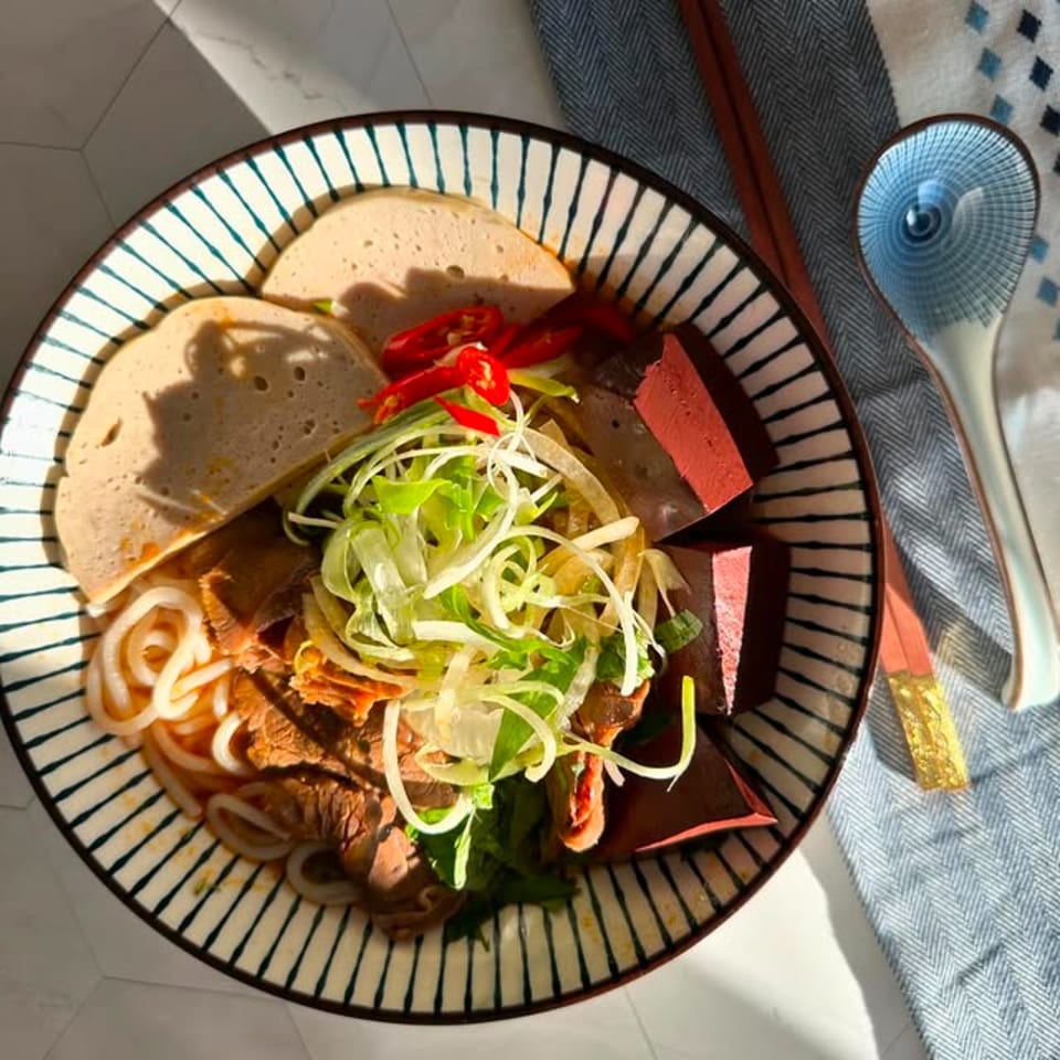 A bowl of Vietnamese Bun Bo Hue with noodles, sliced meat, red chilies, and greens.