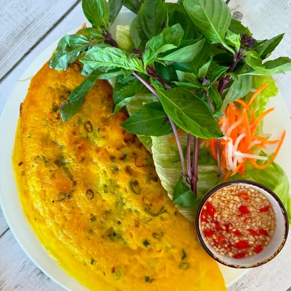 Vietnamese Banh Xeo crepe with fresh herbs, pickled vegetables, and a dipping sauce.