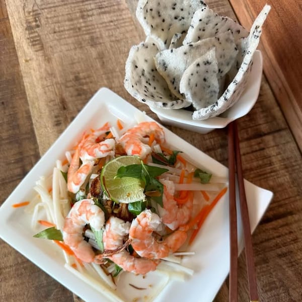 Vietnamese shrimp salad with lime, herbs, and shredded vegetables, served with dragon fruit chips and chopsticks.
