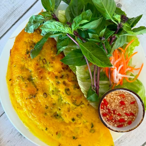 Vietnamese Banh Xeo crepe with fresh herbs, pickled vegetables, and a dipping sauce.