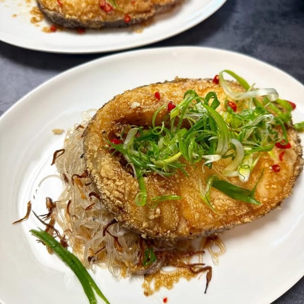 Crispy fried fish fillet with glass noodles, green onions, and red chilies on a white plate.