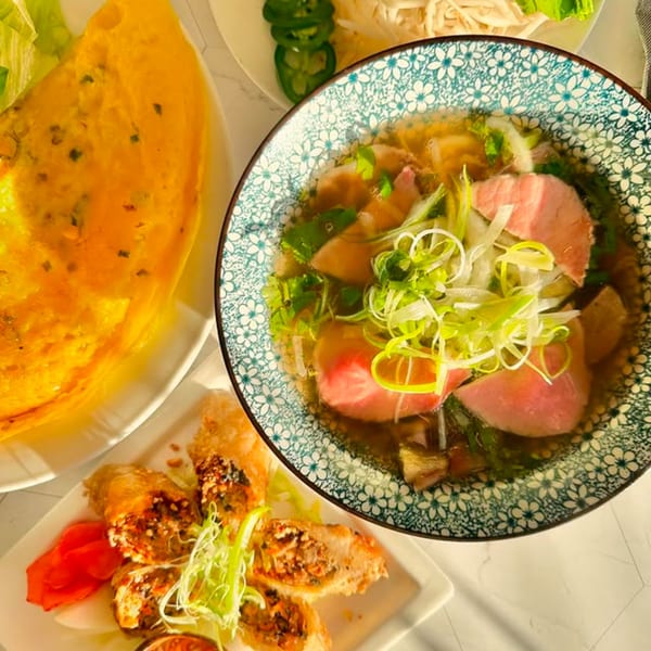 Overhead view of Vietnamese pho, banh xeo, and spring rolls on a white table.
