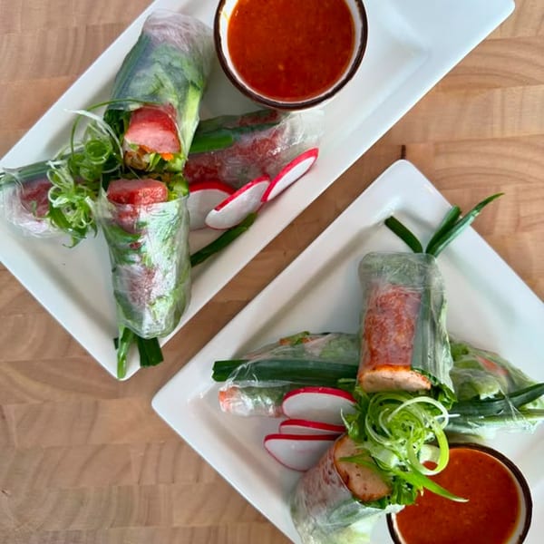 Two plates of fresh Vietnamese spring rolls with red dipping sauce, garnished with radishes and scallions.