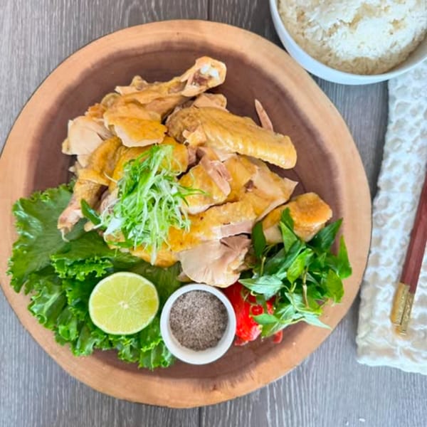 Vietnamese poached chicken with lettuce, lime, herbs, and pepper on a wooden platter.