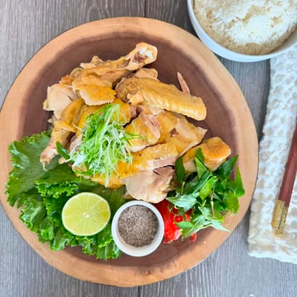 Vietnamese chicken dish with lettuce, lime, herbs, and a side of rice on a wooden platter.