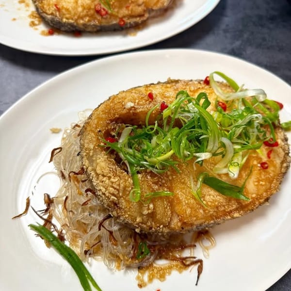 Crispy fried fish steak with glass noodles, green onions, and red chili on a white plate.