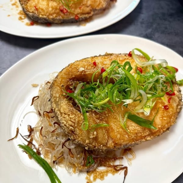 Crispy fried Vietnamese fish steak with vermicelli noodles, green onions, and red chili on a white plate.